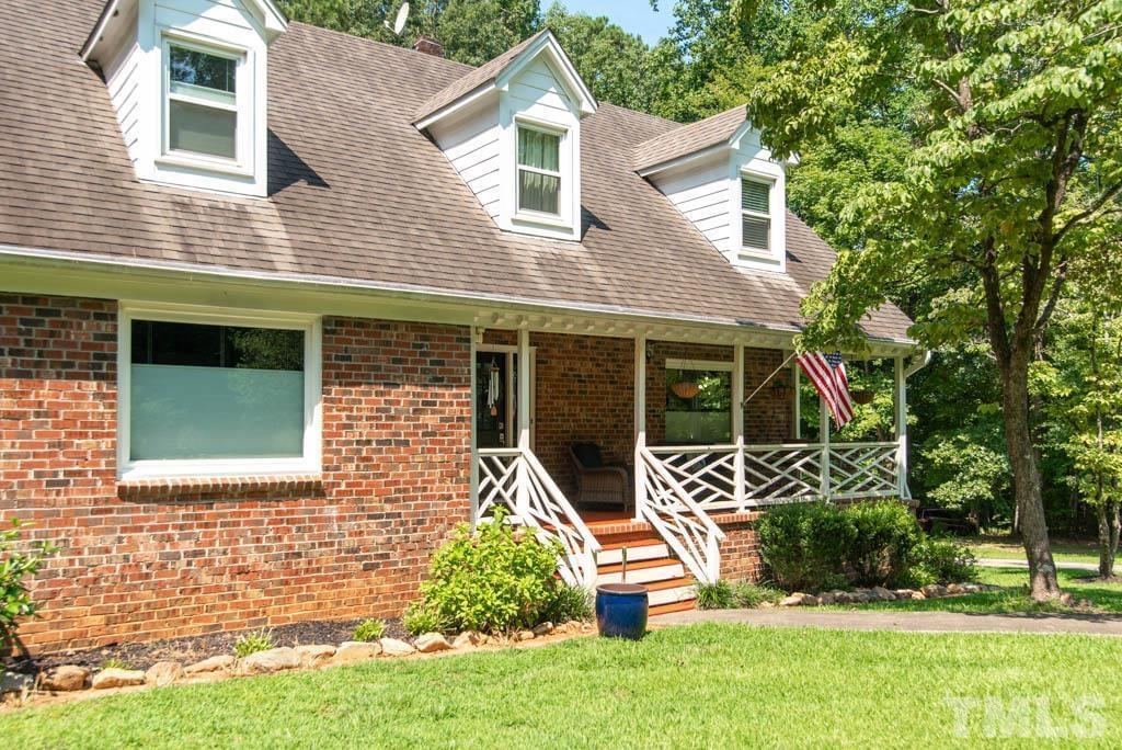 A brick home with a covered porch, white decorative railing, trees out front